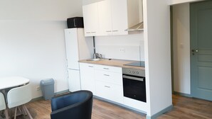 Una cocina compacta con armarios blancos, horno empotrado y un pequeño comedor con mesa y sillas.