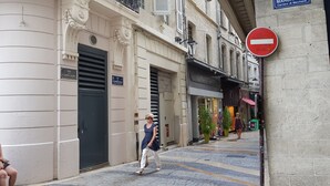 Una calle estrecha flanqueada por edificios, con una señal de 'prohibido el paso' y una mujer caminando.