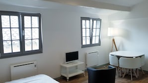 Una habitación de hotel con dos ventanas, un escritorio con computadora, una lámpara, una silla y una cama.