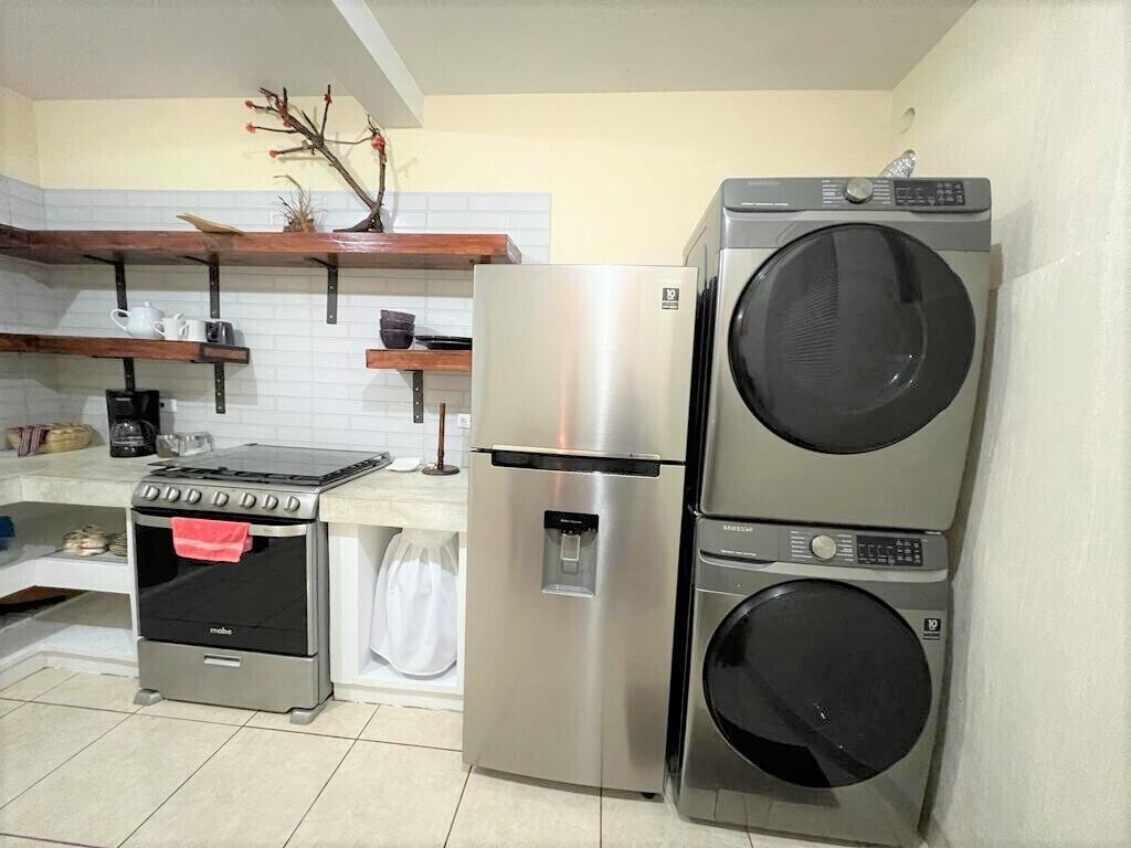 Een praktische keuken met een roestvrijstalen koelkast, een inbouwoven en een gestapelde wasmachine en droger.