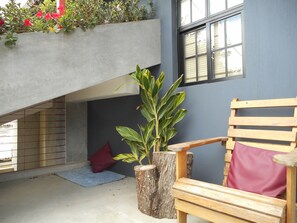 Un banc en bois avec un coussin rouge, une plante en pot et un oreiller rouge posé sur le sol.
