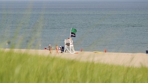 En livredderstand med et flag, strandstole og en gul surfbræt på sandet tæt på vandet.