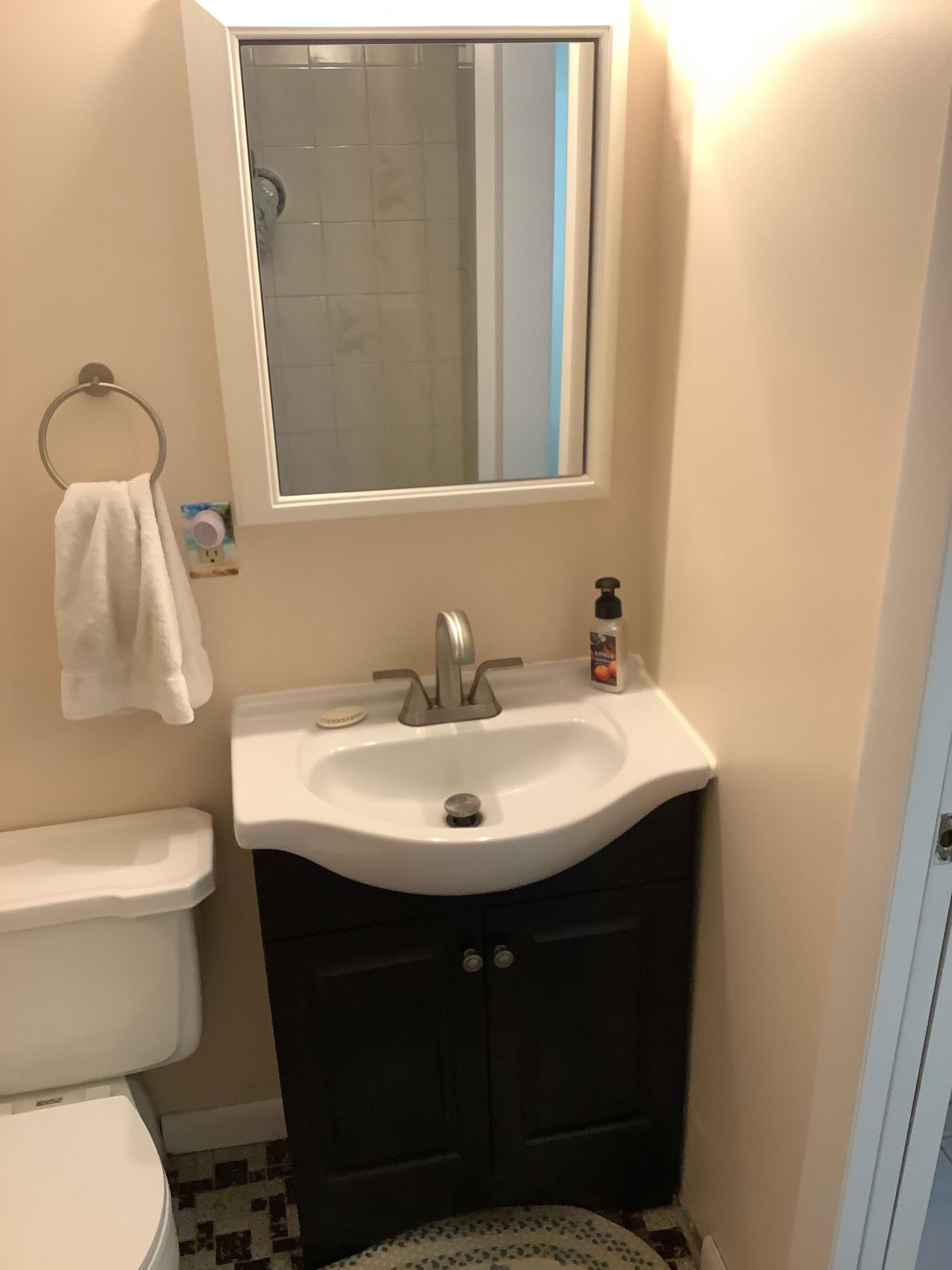 Ein Badezimmer mit einem weißen Waschbecken, dunklen Schränken, einer Toilette und einem Spiegel über dem Waschbecken.
