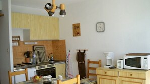 A compact kitchen with a dining table, wooden cabinets, a microwave, a coffee maker, and a vintage radio. - Apartment T2 duplex Font-Romeu (Font-Romeu)