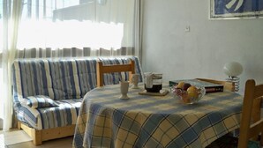 A cozy room with a striped sofa, a round table with a plaid tablecloth, and a bowl of fruit. - Apartment T2 duplex Font-Romeu (Font-Romeu)
