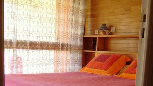 A bedroom with a wooden headboard, a bed with a pink bedspread, orange pillows, and a window with patterned curtains. - Apartment T2 duplex Font-Romeu (Font-Romeu)