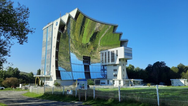 A modern building with a unique curved facade, large windows, and a visible sign indicating a public space. - Apartment T2 duplex Font-Romeu (Font-Romeu)