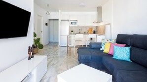 A modern apartment with a living area featuring a dark sofa, a white coffee table, and colorful pillows. A kitchen with white cabinets and a microwave is visible in the background. - Home2Book Sea Views Tabaiba, Wifi & Terrace (Tabaiba)