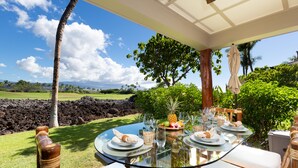 An outdoor dining area with a glass table, white cushions, and a tropical view. - Sophisticated freshly remodeled 3bd+/3ba, two story villa w/ Private Beach club (Puako)