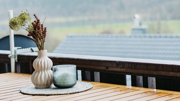 A wooden table with a vase of flowers and a glass on a balcony overlooking a mountainous landscape. - Ferienwohnung mit Seeblick Sport und Erholung (Winterberg)