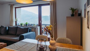 A cozy living room with a sofa, a dining table, and a view of mountains through large windows. - Ferienwohnung mit Seeblick Sport und Erholung (Winterberg)