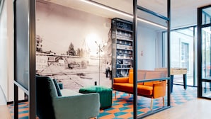 A modern office space with a colorful geometric floor pattern, a large bookshelf, and a foosball table. - YOUNIQ Gdansk - Campus Accommodation (Gdansk)
