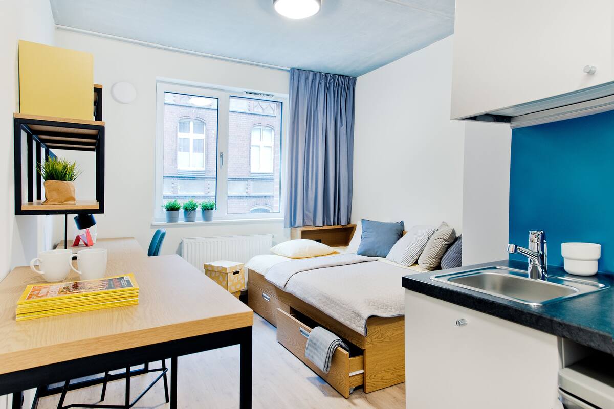 Een knus slaapkamer met een bed, nachtkastje en een kleine kitchenette.