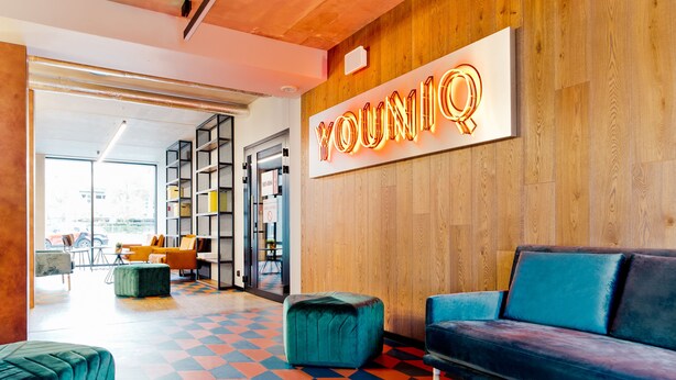 A modern interior with a neon sign reading "YOUNIQ," a blue sofa, a green ottoman, and a colorful geometric floor pattern. - YOUNIQ Gdansk - Campus Accommodation (Gdansk)
