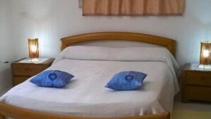 Quarto com cama de madeira, duas luminárias de cabeceira, um tapete amarelo e um quadro na parede.