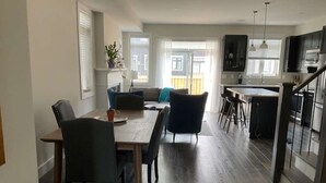 Moderni keittiö, jossa on tummat kaapit, ruokailutila puupöydällä ja -tuoleilla sekä suuret ikkunat, joista on näkymä ulos.