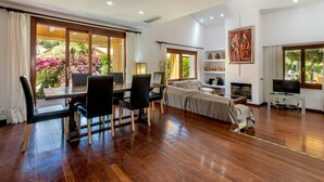 A spacious living area with a wooden floor, a dining table with chairs, a sofa, a television, and a fireplace.