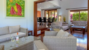 A spacious living area with a glass coffee table, wicker furniture, and a dining area with chairs and a table.