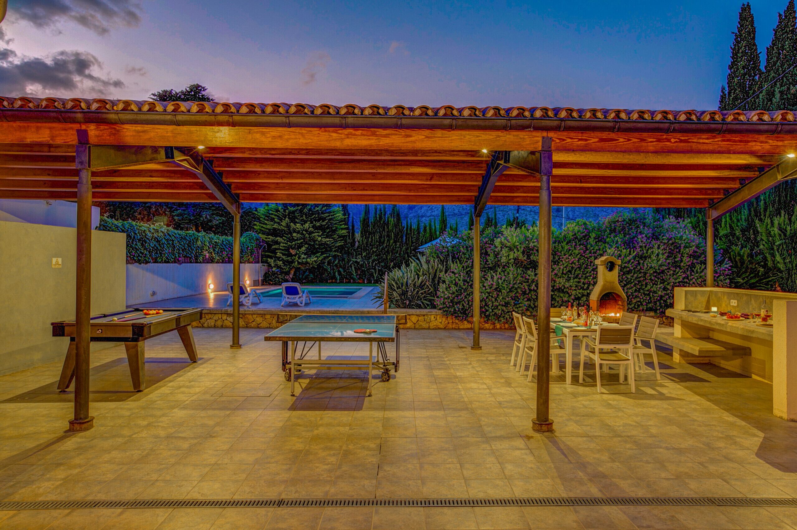 Un patio al aire libre con piscina, mesa, sillas y horno de pizza.