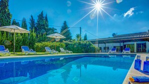 A clear blue swimming pool with lounge chairs and umbrellas, surrounded by greenery and a building with a tiled roof. - Llobiman, Villa-Finca 5StarsHome Mallorca (Pollensa / Pollença)