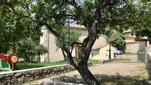 Zona arbolada con un parque infantil, muro de piedra y edificios al fondo.