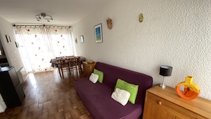 Een woonkamer met een paarse bank, een houten kast en een eethoek met een tafel en stoelen.