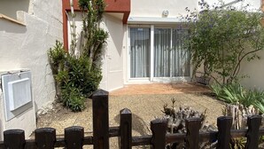 Een gebouw met twee verdiepingen, een gevel in rood en wit, een houten hek en een kleine tuin met planten en een boom.