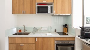 A modern kitchen with wooden cabinets, a microwave, a sink, and an oven. - Le Moulin des Carmélites 1 - Appt moderne à Rennes (Rennes)