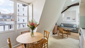Een modern appartement met een eethoek, een zithoek met een bank en een televisie, en een stadszicht door grote ramen.