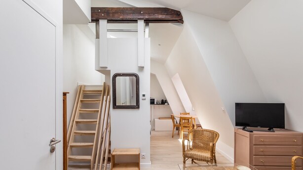 Een modern loft appartement met een schuine plafond, een houten trap, een eetgedeelte met rieten stoelen, een glazen salontafel en een flatscreen televisie.