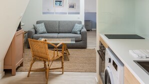 Een knus woongedeelte met een vide, een kitchenette, een eethoek en een grijze bank.