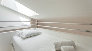 Een moderne slaapkamer met dakraam, een bed met witte lakens en een handdoek op de vloer.