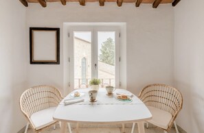 A dining area with a round table, two wicker chairs, a white tablecloth, and a view of a building through a door. - Tusci Loft San Gimignano - Un Piccolo Gioiello nel Città (San Gimignano)