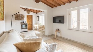 Ein geräumiger Wohnbereich mit hoher Decke, einer Couch, einem Fernseher und einem Essbereich mit Tisch und Stühlen.