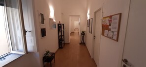 A narrow hallway with a wooden floor, white walls, and a door at the end. There are framed pictures and a bulletin board on the walls. - Casa Laura Oliva Mancini (Napoli)