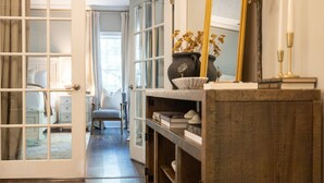 Un couloir avec un plancher en bois, une porte blanche et un miroir posé sur une étagère en bois.