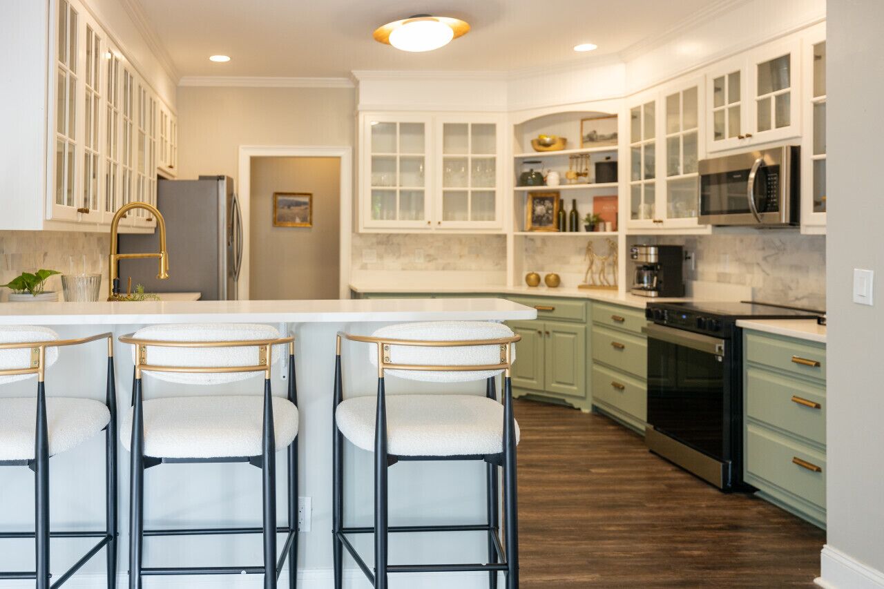 A modern kitchen with white cabinets, a central island with bar stools, stainless steel appliances, and a wooden floor.