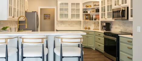 A modern kitchen with white cabinets, a central island with bar stools, stainless steel appliances, and a wooden floor.