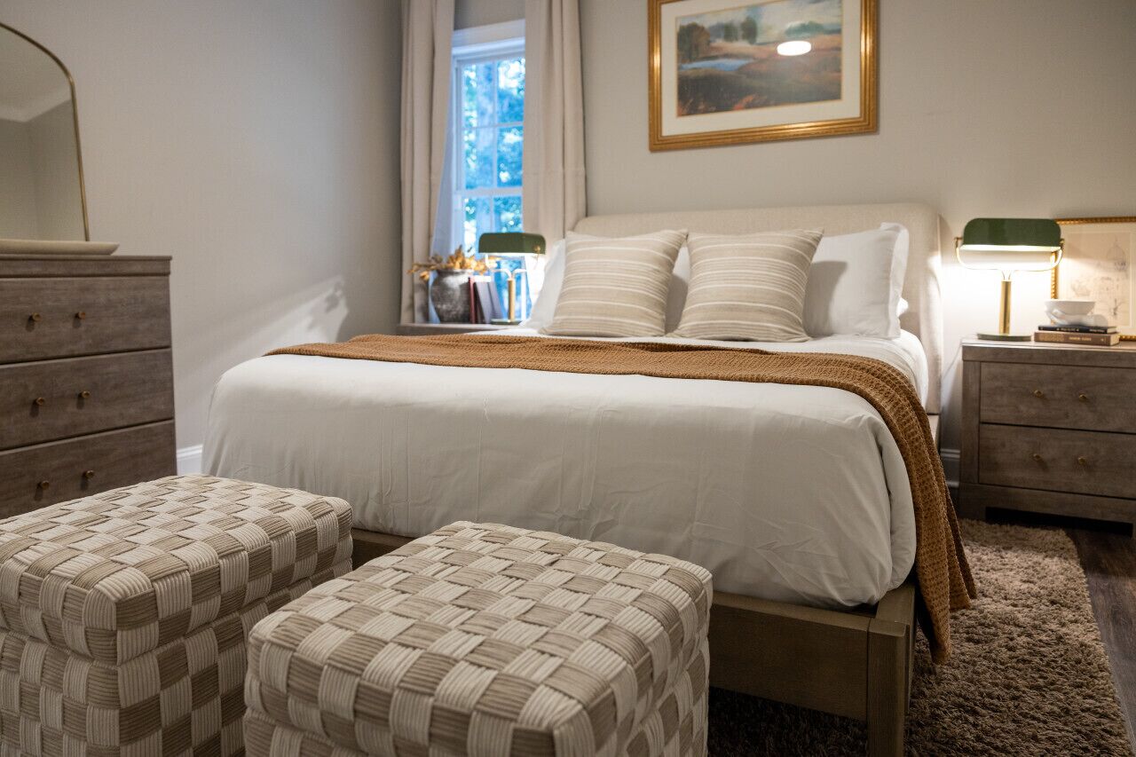 Une chambre à coucher avec un lit, deux tables de chevet, une commode et une fenêtre avec des rideaux.
