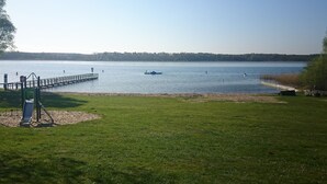 Un césped con un parque infantil y un muelle que se adentra en un lago tranquilo.