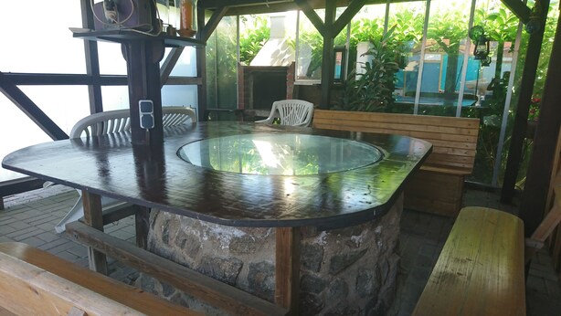 Una mesa redonda con tapa de vidrio y base de piedra, rodeada de bancos y sillas de madera.