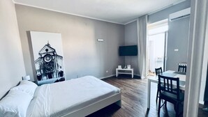 A hotel room with a bed, a desk, a chair, a flat-screen TV, and a large window. - Full house (Bari)