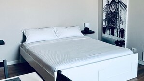 A modern bedroom with a white bed, a nightstand with a lamp, a framed picture on the wall, and a wooden floor. - Full house (Bari)