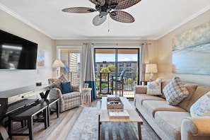 A modern living room with a ceiling fan, a flat-screen TV, a dining table with benches, a sofa, and a coffee table.