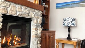 A living room with a stone fireplace, a television mounted above it, a wooden cabinet, and a table with a lamp.