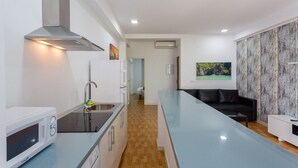 A modern kitchen with a stainless steel range hood, a microwave, and a sink. There is a black leather sofa and a white cabinet in the living area. - El BALNEARIO Apartment by Cadiz4Rentals (Cádiz)