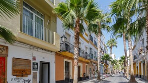 A narrow cobblestone street lined with palm trees and buildings with balconies. - El BALNEARIO Apartment by Cadiz4Rentals (Cádiz)