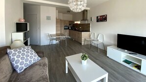 A modern living room with a sofa, coffee table, TV, and a dining area with chairs. - Modern studio with breathtaking view close to the train station (Aix-les-Bains)