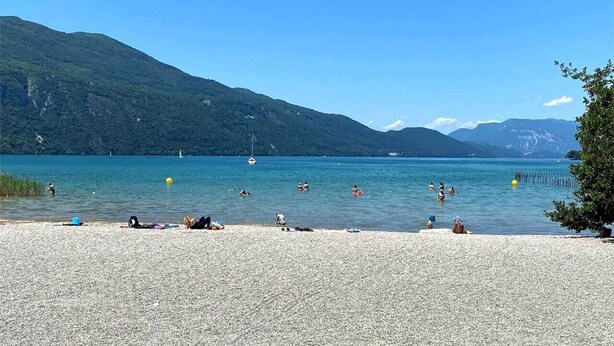 A pebbled beach with people sunbathing and swimming, surrounded by mountains and clear blue water. - Modern studio with breathtaking view close to the train station (Aix-les-Bains)