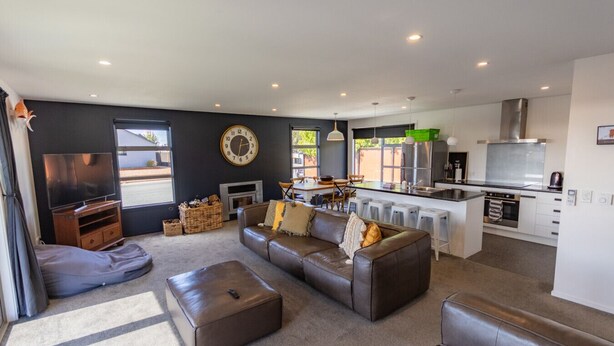A modern living room with a sofa, ottoman, and a flat-screen TV. - Remarkable  Rhoboro Retreat (Twizel)